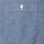 The pocket of the blue chambray work shirt with white buttons.